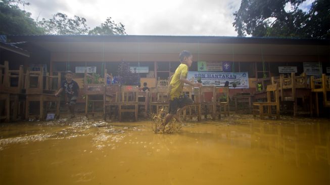 Dua orang murid bermain di lapangan SD Negeri Hantakan yang dipenuhi lumpur akibat meluapnya sungai Hantakan di Kecamatan Hantakan, Kabupaten Hulu Sungai Tengah, Kalimantan Selatan, Jumat (19/11/2021). [ANTARA FOTO/Bayu Pratama S]