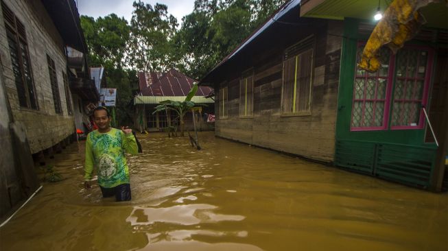 Warga berjalan melintasi banjir yang kembali merendam permukiman di Kecamatan Barabai, Kabupaten Hulu Sungai Tengah, Kalimantan Selatan, Jumat (19/11/2021). [ANTARA FOTO/Bayu Pratama S]