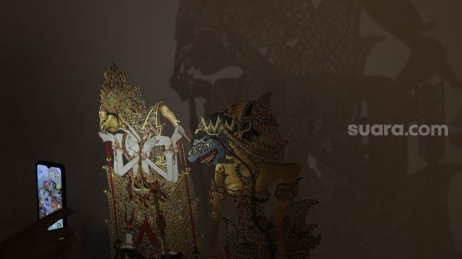 Pengunjung menyinari koleksi wayang menggunakan lampu saat pameran wayang bertema 'Wayang Rupa Kita' di Bentara Budaya, Palmerah, Jakarta, Sabtu (20/11/2021). [Suara.com/Angga Budhiyanto]