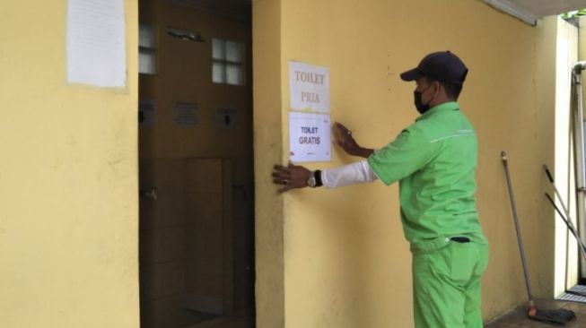 Seorang petugas SPBU di Bandung Barat memasang tanda pengumuman toilet gratis. [Suara.com/Ferrye Bangkit Rizki]