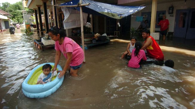 Warga bersama anaknya bermain digenangan air saat terjadi banjir di Kelurahan Pesurungan, Tegal, Jawa Tengah, Selasa (23/11/2021).  ANTARA FOTO/Oky Lukmansya