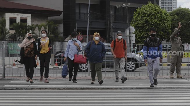 Pekerja menyeberang di 'pelican cross' Tosari saat jam pulang kerja di Jakarta, Selasa (23/11/2021). [Suara.com/Angga Budhiyanto]