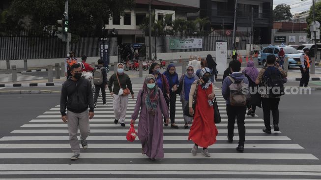 Pekerja menyeberang di 'pelican cross' Tosari saat jam pulang kerja di Jakarta, Selasa (23/11/2021). [Suara.com/Angga Budhiyanto]