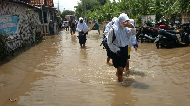 Sejumlah pelajar melintasi genangan air saat terjadi banjir di Kelurahan Pesurungan, Tegal, Jawa Tengah, Selasa (23/11/2021). ANTARA FOTO/Oky Lukmansya