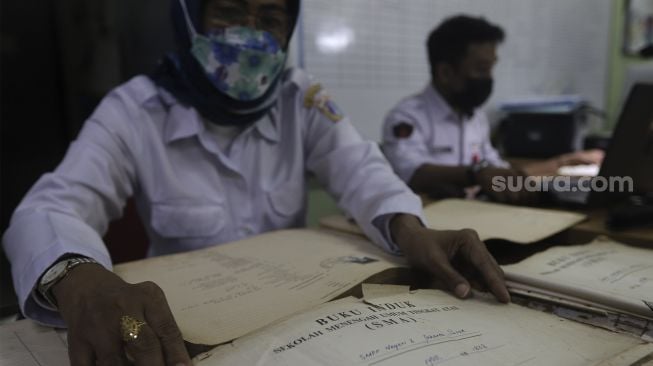 Petugas Dinas Perpustakaan dan Kearsipan (Dispusip) Provinsi DKI Jakarta menyiapkan buku induk sekolah untuk didigitalisasikan di SMAN 77, Cempaka Putih, Jakarta, Rabu (24/11/2021). [Suara.com/Angga Budhiyanto]