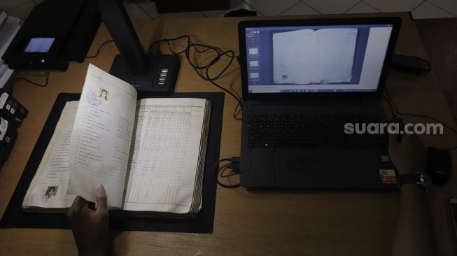 Petugas Dinas Perpustakaan dan Kearsipan (Dispusip) Provinsi DKI Jakarta mendigitalisasikan arsip sekolah di SMAN 77, Cempaka Putih, Jakarta, Rabu (24/11/2021). [Suara.com/Angga Budhiyanto]