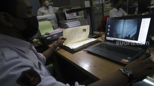 Petugas Dinas Perpustakaan dan Kearsipan (Dispusip) Provinsi DKI Jakarta mendigitalisasikan arsip sekolah di SMAN 77, Cempaka Putih, Jakarta, Rabu (24/11/2021). [Suara.com/Angga Budhiyanto]