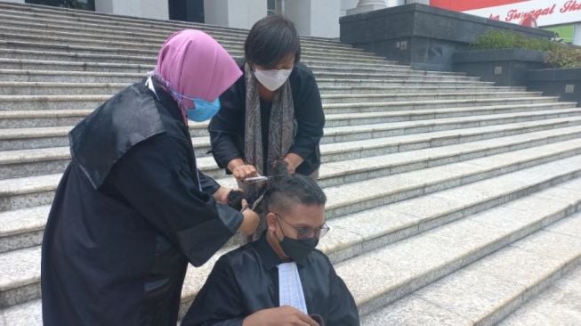 Kuasa hukum penggugat UU Cipta Kerja Viktor Santosa Tandiasa potong rambut usai sidang di Mahkamah Konstitusi (MK) pada Kamis (25/11/2021). [Suara.com/Yaumal]