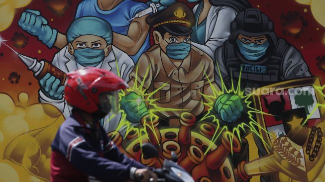 Pengendara sepeda motor melintas di depan mural bertema COVID-19 di Jakarta, Jumat (26/11/2021). [Suara.com/Angga Budhiyanto]