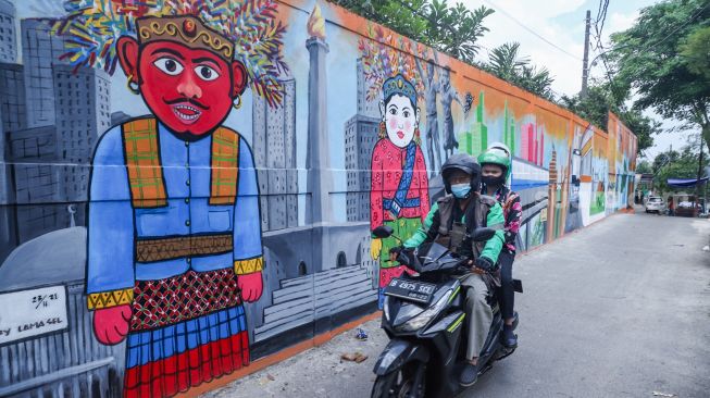 Pengendara motor melintas di depan mural dengan tema Jakarta di Kebayoran Lama, Jakarta Selatan, Jumat (26/11/2021). [Suara.com/Alfian Winanto]