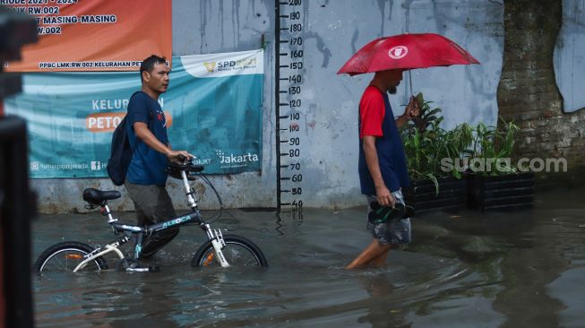 Warga melintasi banjir di Jalan Wijaya Timur, Petogogan, Jakarta Selatan, Jumat (26/11/2021). [Suara.com/Alfian Winanto]