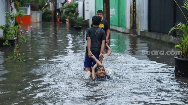 Anak - anak bermain banjir di Jalan Wijaya Timur, Petogogan, Jakarta Selatan, Jumat (26/11/2021). [Suara.com/Alfian Winanto]