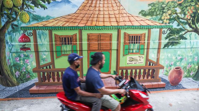 Pengendara motor melintas di depan mural dengan tema Jakarta di Kebayoran Lama, Jakarta Selatan, Jumat (26/11/2021). [Suara.com/Alfian Winanto]