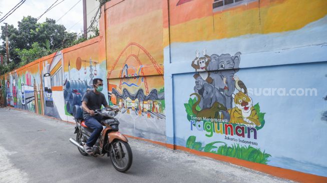 Pengendara motor melintas di depan mural dengan tema Jakarta di Kebayoran Lama, Jakarta Selatan, Jumat (26/11/2021). [Suara.com/Alfian Winanto]