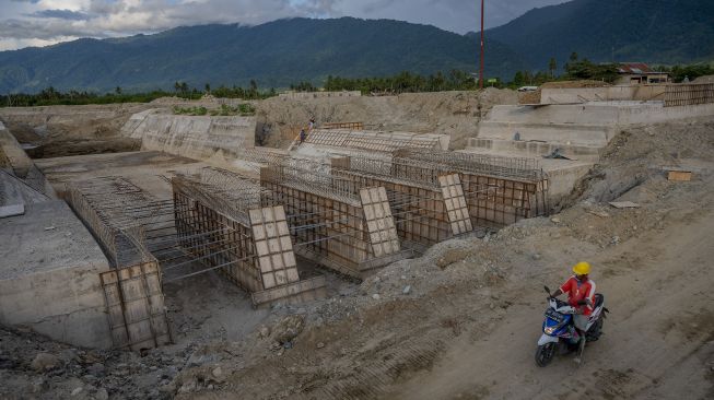 Pengendara sepeda motor melintas di dekat proyek saluran air pengendali banjir di Desa Bangga, Sigi, Sulawesi Tengah, Jumat (26/11/2021). [ANTARA FOTO/Basri Marzuki]