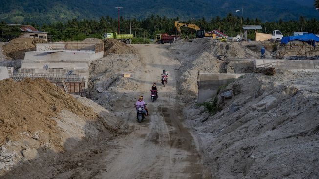 Pengendara sepeda motor melintas di dekat proyek saluran air pengendali banjir di Desa Bangga, Sigi, Sulawesi Tengah, Jumat (26/11/2021). [ANTARA FOTO/Basri Marzuki]