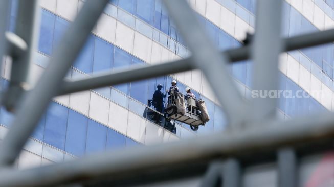 Pekerja membersihkan dan melakukan perawatan bagian kaca luar salah satu gedung bertingkat di kawasan Jakarta Selatan, Minggu (28/11/2021). [Suara.com/Alfian Winanto]