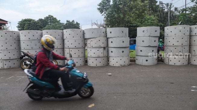 Warga melintas di dekat buis beton drainase vertikal di kawasan Manggarai, Jakarta Selatan, Selasa (30/11/2021). [Suara.com/Alfian Winanto]