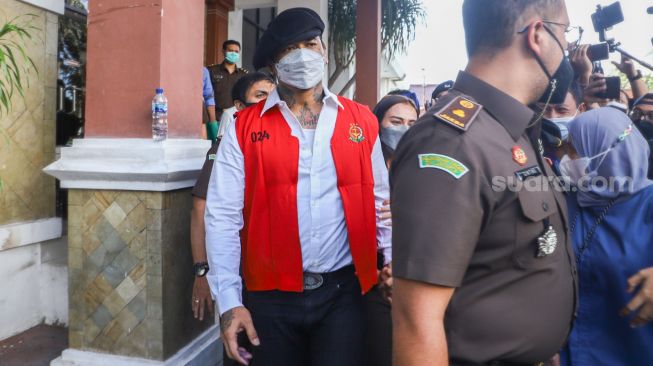 Musisi I Gede Ari Astina atau Jerinx SID berjalan keluar mengenakan rompi tahanan berwarna merah usai menjalani pemeriksaan di Kejaksaan Negeri Jakarta Pusat, Rabu (1/12/2021). [Suara.com/Alfian Winanto]