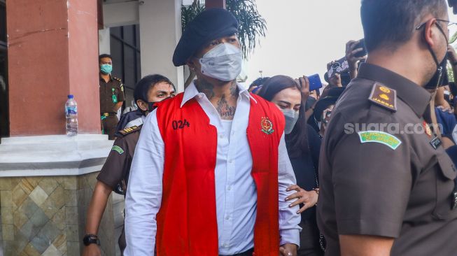 Musisi I Gede Ari Astina atau Jerinx SID berjalan keluar mengenakan rompi tahanan berwarna merah usai menjalani pemeriksaan di Kejaksaan Negeri Jakarta Pusat, Rabu (1/12/2021). [Suara.com/Alfian Winanto]