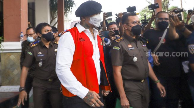 Musisi I Gede Ari Astina atau Jerinx SID berjalan keluar mengenakan rompi tahanan berwarna merah usai menjalani pemeriksaan di Kejaksaan Negeri Jakarta Pusat, Rabu (1/12/2021). [Suara.com/Alfian Winanto]