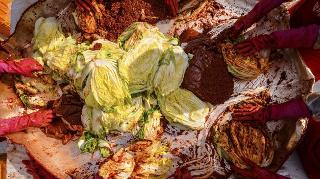 Para peserta menyiapkan kimchi, hidangan tradisional Korea dari kubis dan lobak pedas yang difermentasi, selama festival pembuatan kimchi di kuil Buddha Jogyesa, Seoul, Korea Selatan, pada (2/12/2021). [ANTHONY WALLACE / AFP]