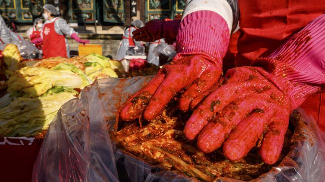 Para peserta menyiapkan kimchi, hidangan tradisional Korea dari kubis dan lobak pedas yang difermentasi, selama festival pembuatan kimchi di kuil Buddha Jogyesa, Seoul, Korea Selatan, pada (2/12/2021). [ANTHONY WALLACE / AFP]