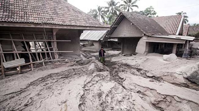 Warga melintas di rumah yang rusak akibat abu vulkanik letusan Gunung Semeru di Desa Sumber Wuluh, Lumajang, Jawa Timur, Minggu (5/12/2021). [Antara/Umarul Faruq]