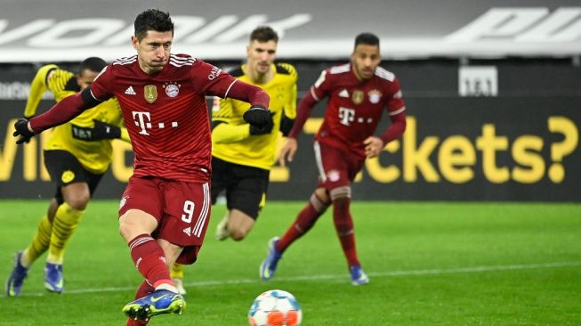 Aksi striker Robert Lewandowski mencetak gol penalti memastikan kemenangan 3-2 Bayern Muenchen di kandang rival berat mereka Borussia Dortmund, Minggu (5/12/2021) dini hari WIB. (Foto: AFP)