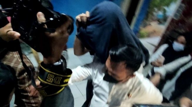 Tersangka AR, dosen Unsri, menutupi mukanya menggunakan jaket ketika digiring keluar dari ruang penyidikan di Mapolda Sumsel, Senin (6/12/2021). [ANTARA] 