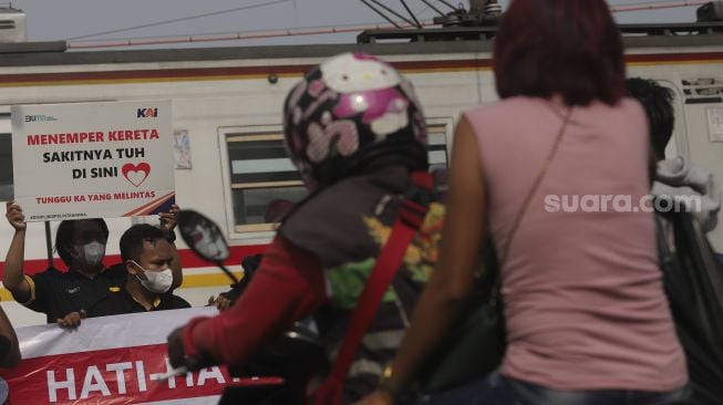 Petugas dan relawan dari komunitas Railfans melakukan sosialisasi keselamatan di perlintasan sebidang Bukit Duri, Jakarta, Sabtu (11/12/2021). [Suara.com/Angga Budhiyanto]