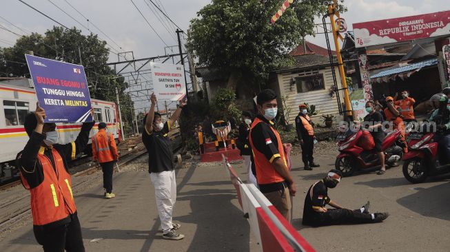 Petugas dan relawan dari komunitas Railfans melakukan sosialisasi keselamatan di perlintasan sebidang Bukit Duri, Jakarta, Sabtu (11/12/2021). [Suara.com/Angga Budhiyanto]