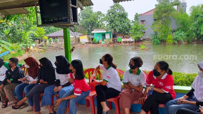 Para remaja KBA Pinang mendengarkan wejangan dari tamu pembicara, Ketua RW 06, dan Sekretaris RW 06 serta para pengurus Proklim. Perhatikan latar belakang Kali Angke yang tengah meninggi [Suara.com/CNR ukirsari].