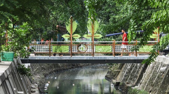 Warga melintasi jembatan di Jalan Galur Sari Timur, Matraman, Jakarta Timur, Senin (13/12/2021). [Suara.com/Alfian Winanto]