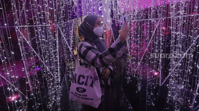 Pengunjung berswafoto di dalam dekorasi perayaan Natal bertema "A Shining Shimmering Christmas" di Mal Grand Indonesia, Jakarta, Senin (13/12/2021). [Suara.com/Angga Budhiyanto]