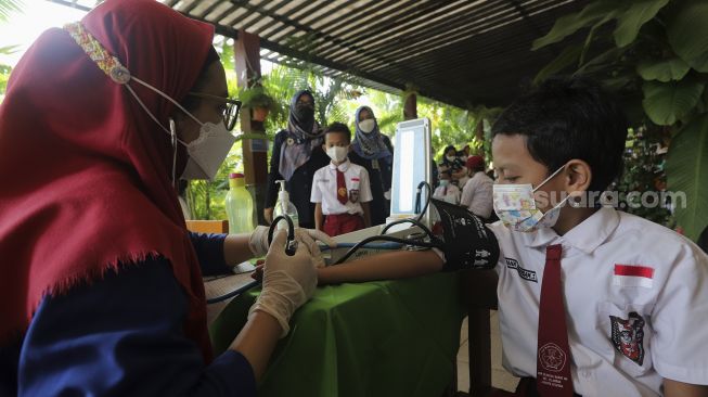 Tenaga kesehatan memeriksa kondisi kesehatan pelajar sebelum mendapatkan vaksin COVID-19 di SDN 04 Cilandak Barat, Jakarta, Selasa (14/12/2021). [Suara.com/Angga Budhiyanto]