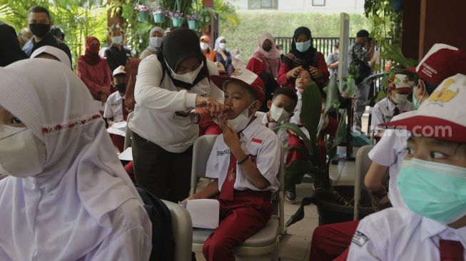 Orang tua memberikan minum kepada anaknya sebelum mendapatkan vaksin COVID-19 kepada pelajar di SDN 04 Cilandak Barat, Jakarta, Selasa (14/12/2021). [Suara.com/Angga Budhiyanto]