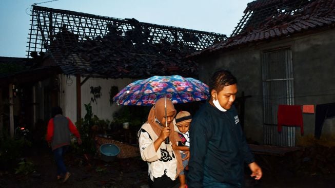 Sejumlah orang melintas di dekat bangunan rumah yang rusak akibat puting beliung di Wonoasri, Kabupaten Madiun, Jawa Timur, Rabu (15/2/2021). ANTARA FOTO/Siswowidodo
