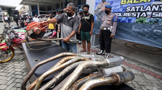 Petugas menyaksikan pemotongan knalpot yang tidak standar atau "brong" hasil razia balap liar motor di halaman Polresta Sidoarjo, Jawa Timur, Sabtu (18/12/2021). ANTARA FOTO/Umarul Faruq
