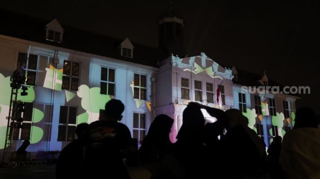 Sejumlah pengunjung melihat video mapping bernuansa Natal yang ditampilkan dalam acara 'Christmas in Jakarta' di Museum Fatahillah, Kota Tua, Jakarta, Minggu (19/12/2021). [Suara.com/Angga Budhiyanto]