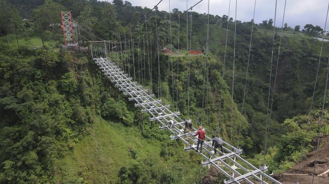 Sejumlah pekerja membawa kerangka besi saat membangun jembatan gantung di lereng Gunung Merapi, Tegalmulyo, Kemalang, Klaten, Jawa Tengah, Sabtu (18/12/2021). [ANTARA FOTO/Aloysius Jarot Nugroho]