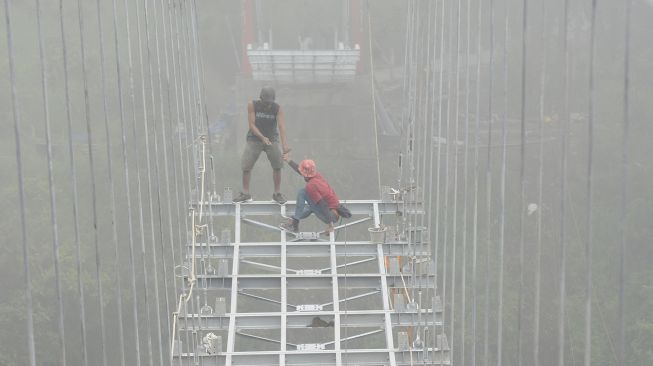 Sejumlah pekerja memasang kerangka besi saat membangun jembatan gantung di lereng Gunung Merapi, Tegalmulyo, Kemalang, Klaten, Jawa Tengah, Sabtu (18/12/2021). [ANTARA FOTO/Aloysius Jarot Nugroho]