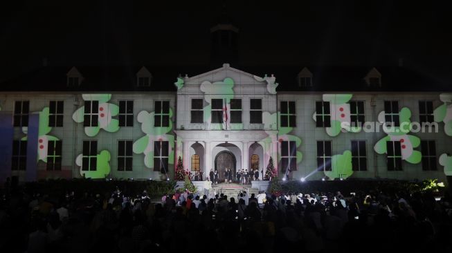 Sejumlah pengunjung melihat video mapping bernuansa Natal yang ditampilkan dalam acara 'Christmas in Jakarta' di Museum Fatahillah, Kota Tua, Jakarta, Minggu (19/12/2021). [Suara.com/Angga Budhiyanto]