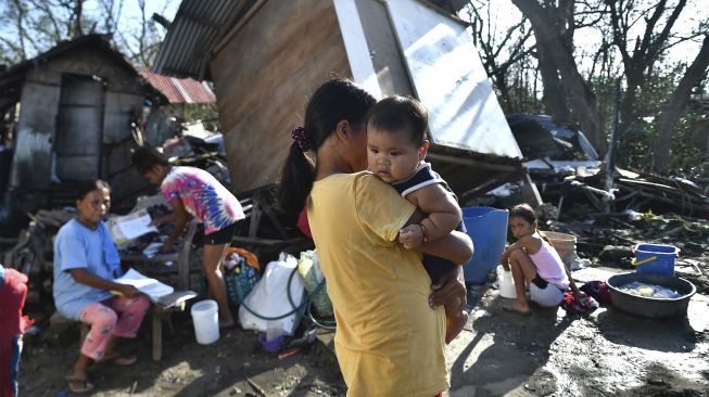 Warga berkumpul di sebelah rumah mereka yang hancur di Carcar, Provinsi Cebu, Filipina, pada (18/12/2021). [VICTOR KINTANAR / AFP]