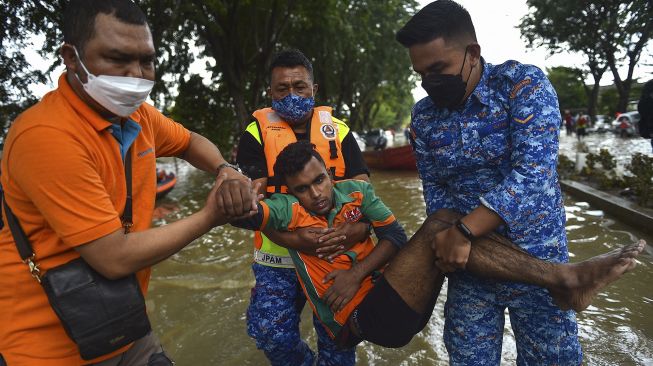 Anggota Departemen Pertahanan Sipil Malaysia membawa seorang pria yang terjebak banjir di Shah Alam, Selangor, Malaysia, Senin (20/12/2021). [ARIF KARTONO / AFP]