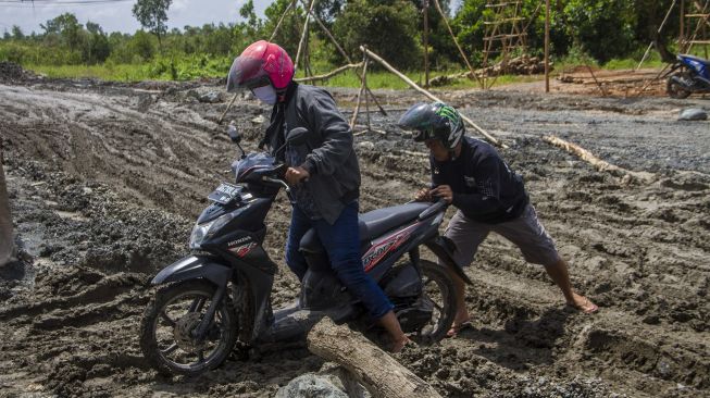 Warga mendorong sepeda motornya yang terjebak di jalan Trans Kalimantan yang rusak di Kecamatan Liang Anggang, Banjarbaru, Kalimantan Selatan, Minggu (19/12/2021). [ANTARA FOTO/Bayu Pratama S]