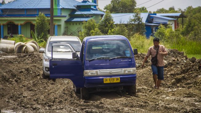 Warga melihat mobilnya yang terjebak di jalan Trans Kalimantan yang rusak di Kecamatan Liang Anggang, Banjarbaru, Kalimantan Selatan, Minggu (19/12/2021). [ANTARA FOTO/Bayu Pratama S]