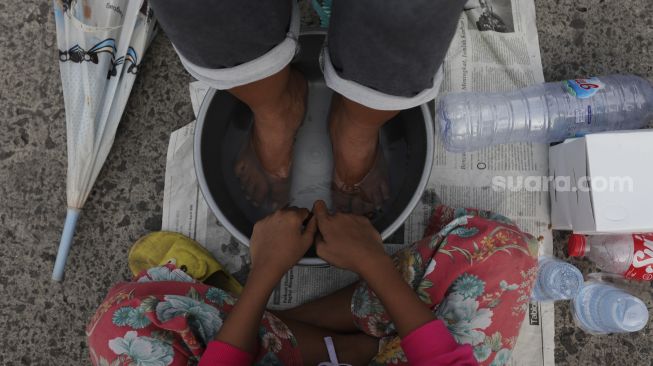 Seorang anak bersiap membasuh kaki ibunya saat acara Cuci Kaki Ibu Massal di Kelurahan Duri Pulo, Gambir, Jakarta, Rabu (22/12/2021). [Suara.com/Angga Budhiyanto]