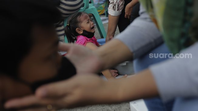 Seorang anak menangis saat membasuh kaki ibunya dalam acara Cuci Kaki Ibu Massal di Kelurahan Duri Pulo, Gambir, Jakarta, Rabu (22/12/2021). [Suara.com/Angga Budhiyanto]