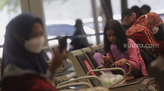 Seorang anak memainkan gawai pintarnya saat menunggu kedatangan kereta api di Stasiun Pasar Senen, Jakarta, Jumat (24/12/2021). [Suara.com/Angga Budhiyanto]